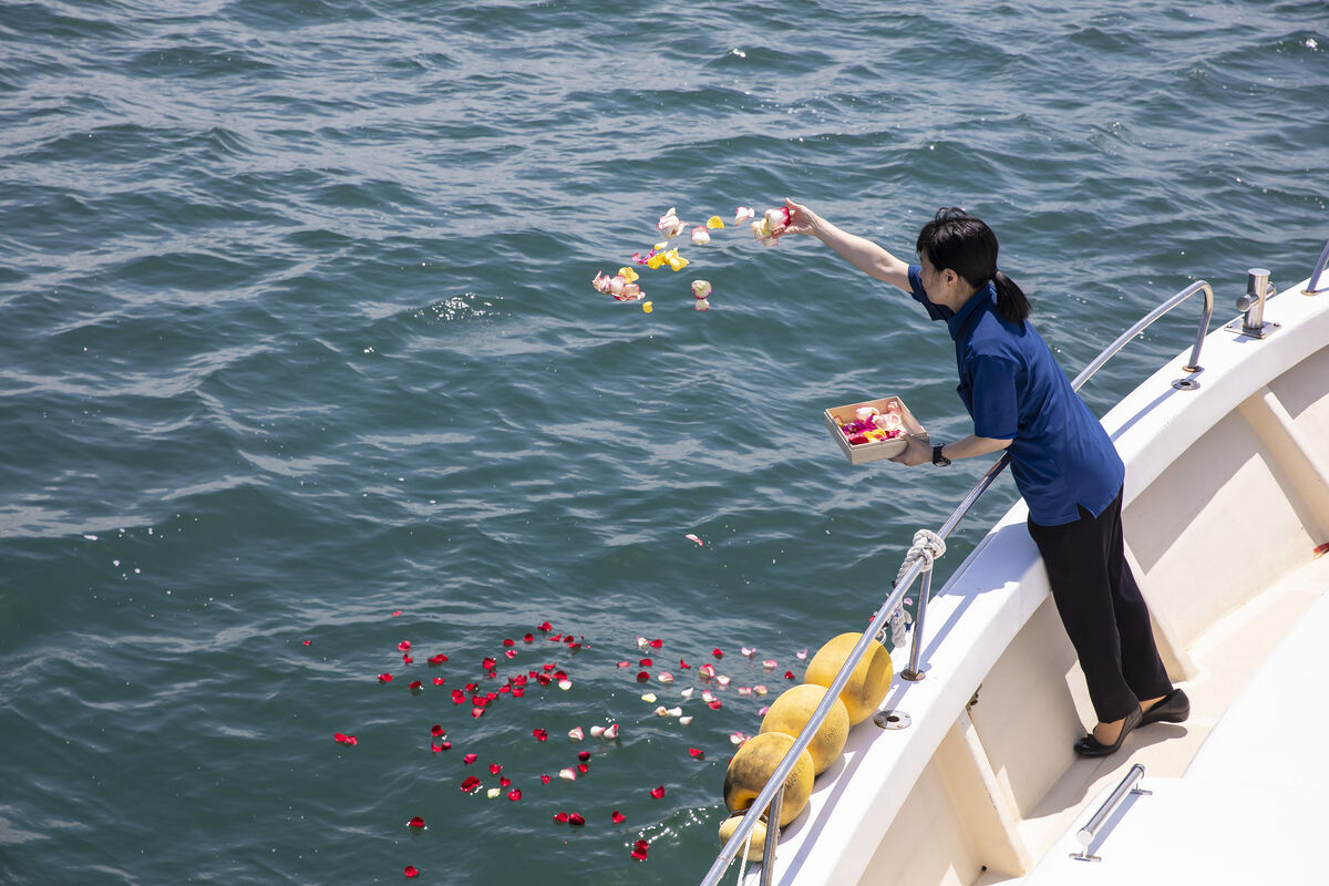 花びらが広がる海と散骨セレモニーを行う船上のスタッフ